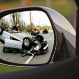 a car's driverside rearview mirror with an overturned car accident in the reflection