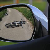Bicycle sitting on the ground, turned over, from the rearview mirror of a car